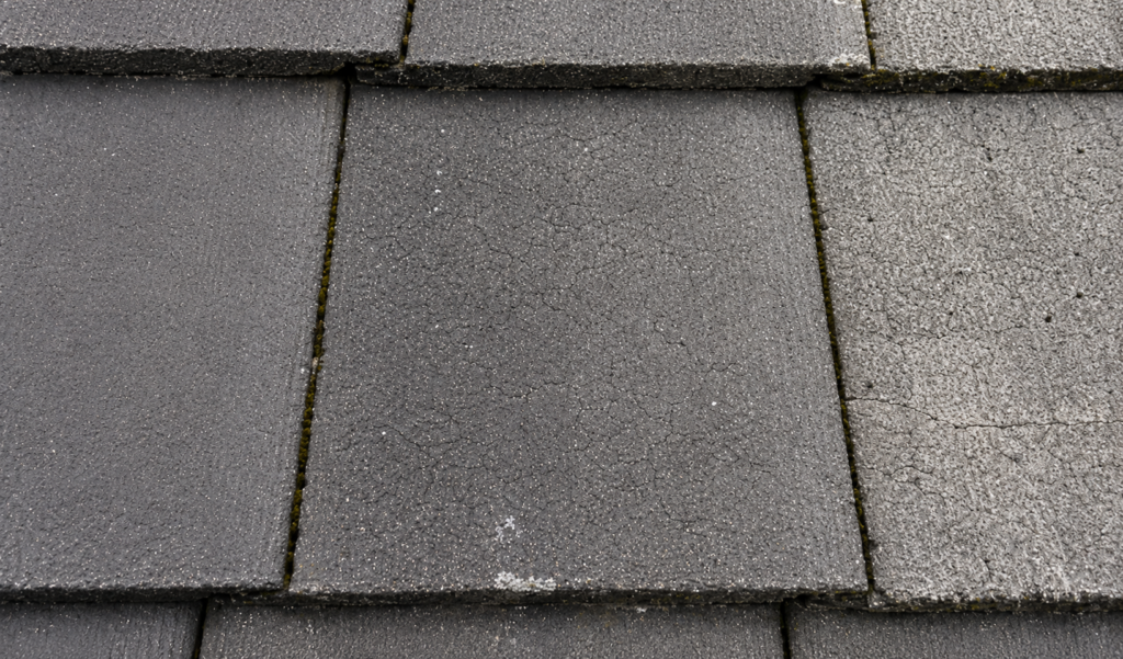 “Close-up of weathered concrete roof tiles showing surface wear, fading, and minor cracking on a pitched residential roof.”