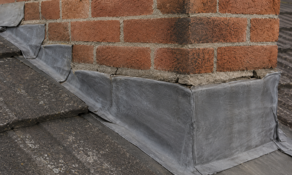 “Close-up of lead flashing installed around a brick chimney stack on a tiled roof, showing weathered mortar joints and roof detailing.”
