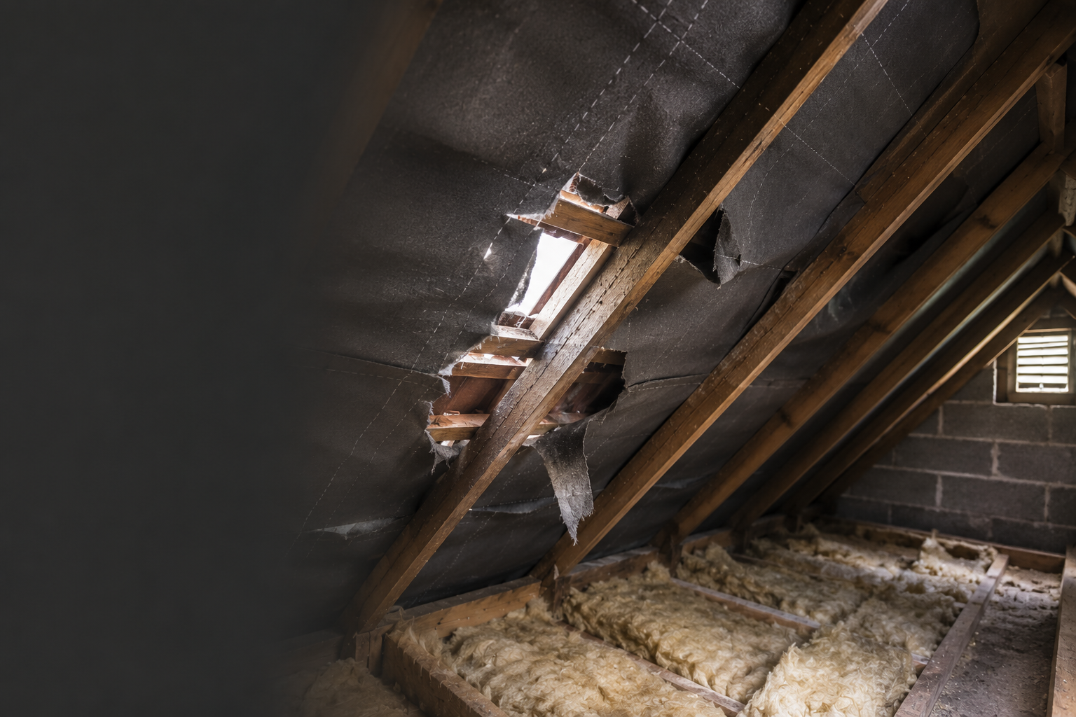 Torn roof underlay visible inside a loft beneath a traditional pitched roof structure